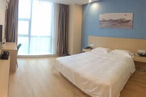 A hotel room with a bed, a desk, a chair, a nightstand, a lamp, and a window with curtains. - Citi Home Hotel (Taohua Town Government) (Feixi)