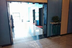 A hallway with a door leading to a room, a potted plant, and a trash bin. - Citi Home Hotel (Taohua Town Government) (Feixi)