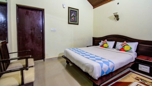 Una habitación de hotel con una cama de madera, una silla, una puerta y una lámpara fijada a la pared.