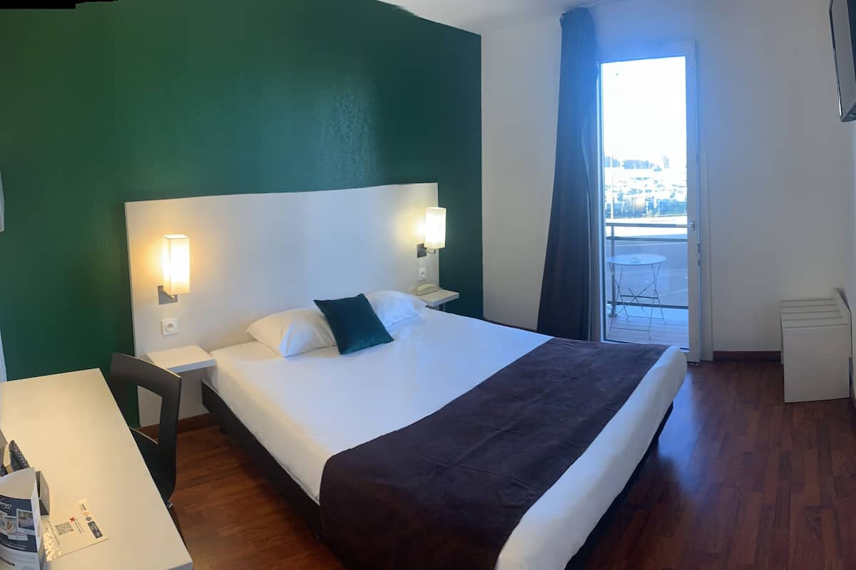 Una habitación de hotel con cama, mesitas de noche, ventana con vistas y una puerta.