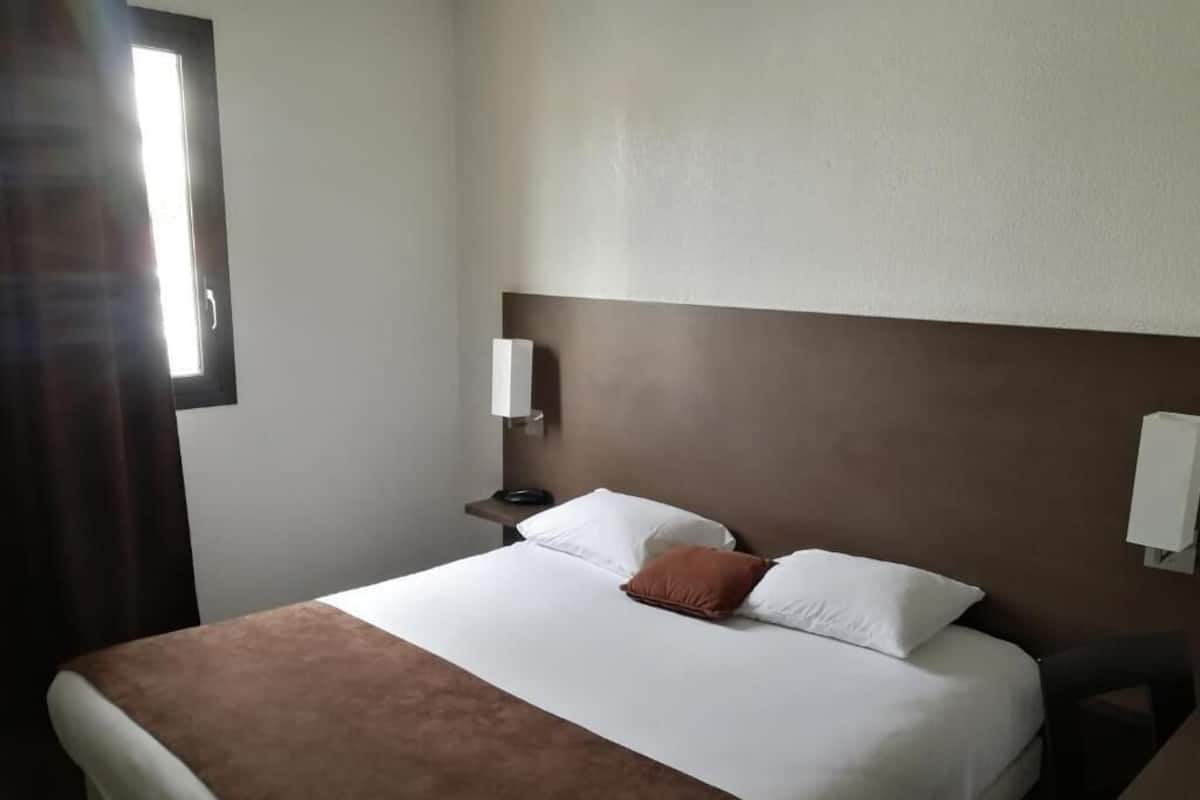 Una habitación de hotel con una cama grande, una mesita de noche y una lámpara de pared.