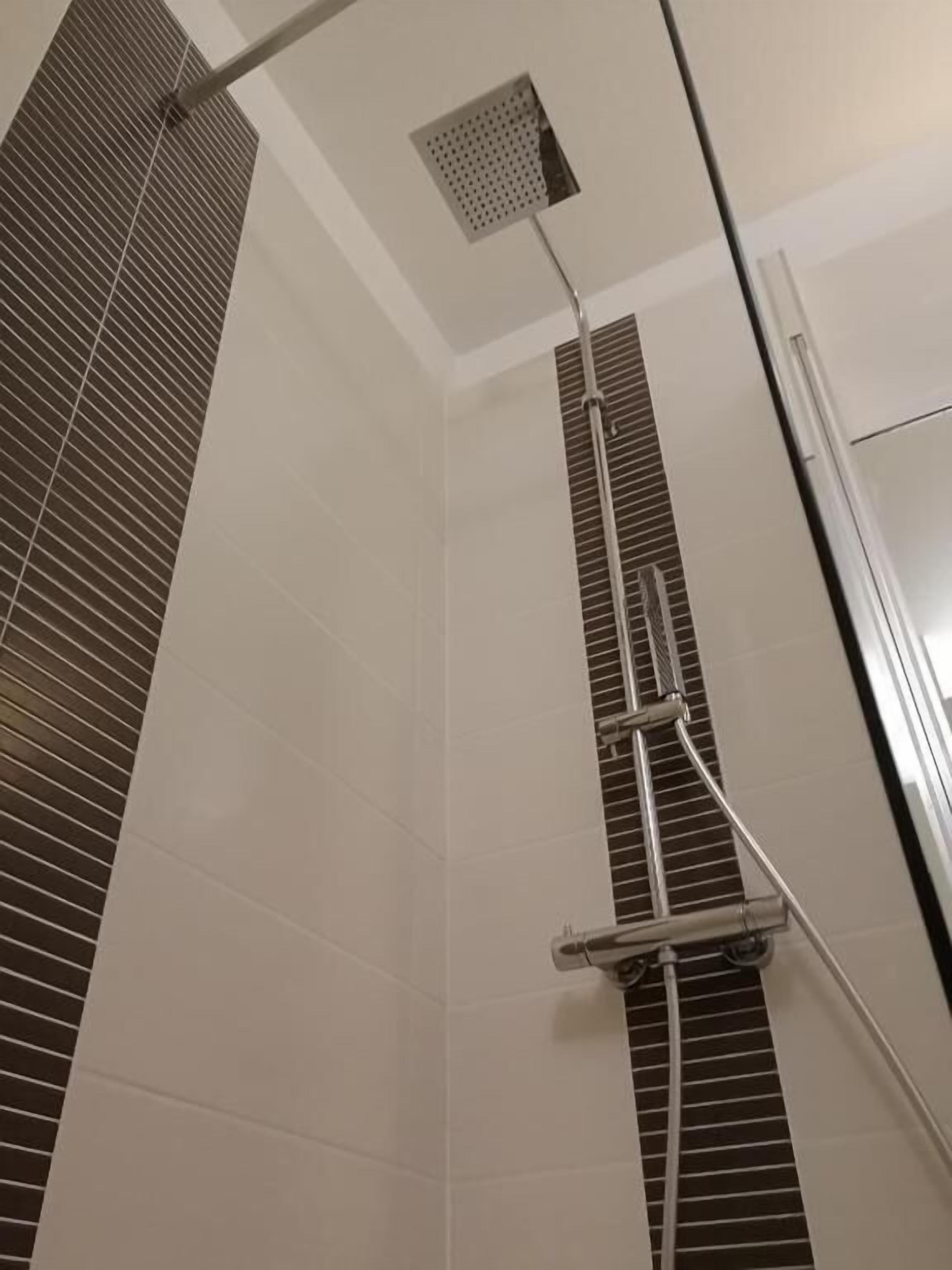 A shower with a metal rain showerhead and a square vent on the ceiling.