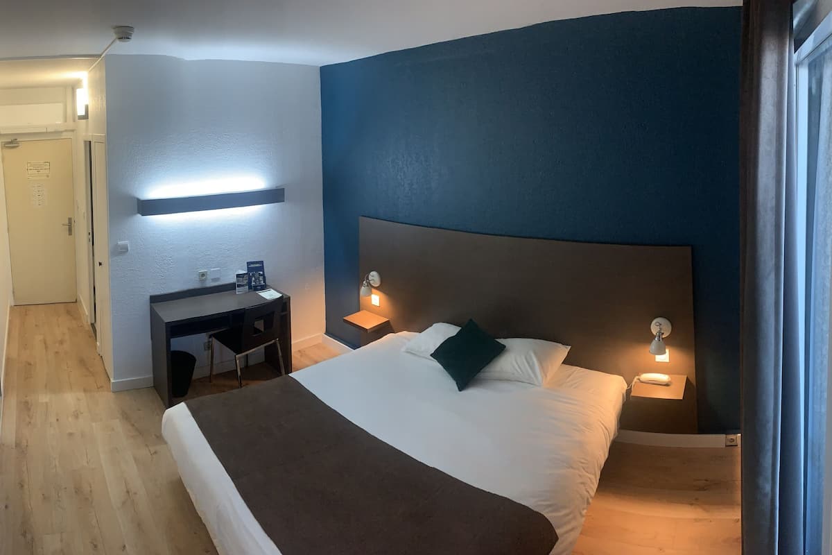 Una habitación de hotel con cama, lámparas de noche, un escritorio y una silla.