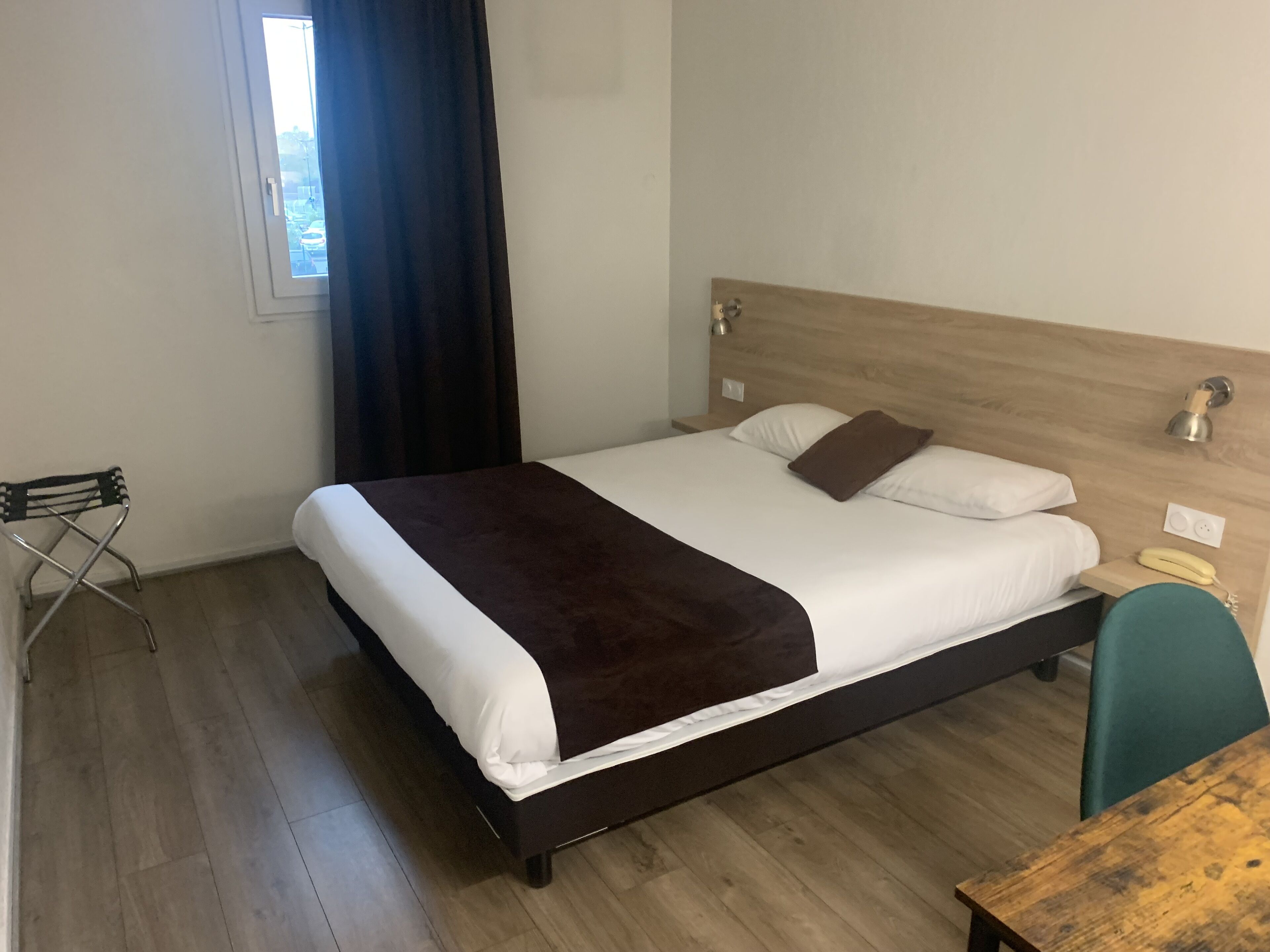 Una cama bien hecha con un edredón marrón oscuro, un cabecero de madera y una lámpara de noche.