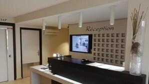 Un mostrador de recepción con un televisor de pantalla plana, un panel informativo en la pared y un jarrón decorativo.