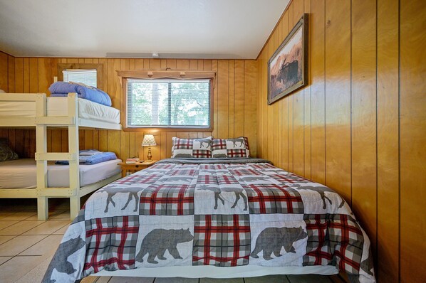 Une chambre avec un lit superposé, une couverture à carreaux, des murs en bois, une fenêtre avec des stores et une table de chevet avec une lampe.