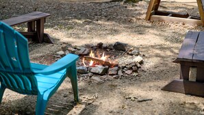 Un camping con un hoyo para fuego rodeado de rocas, dos bancos de madera y una silla turquesa.