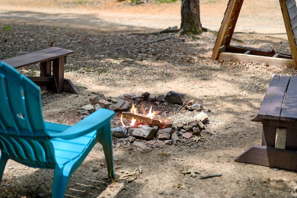 Ein Campingplatz mit Feuerstelle, umgeben von Steinen, zwei Holzbanken und einem türkisfarbenen Stuhl.