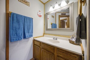 Ein Badezimmer mit einem weißen Waschbecken, Holzschränken, einem Spiegel und zwei blauen Handtüchern, die an der Wand hängen.