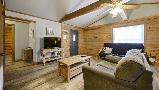 A wooden-floored living room with a sofa, a coffee table, a television, and a ceiling fan.