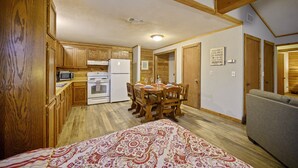 Una cocina compacta con armarios de madera, microondas y refrigerador. Hay una mesa de comedor con sillas y una colcha estampada.