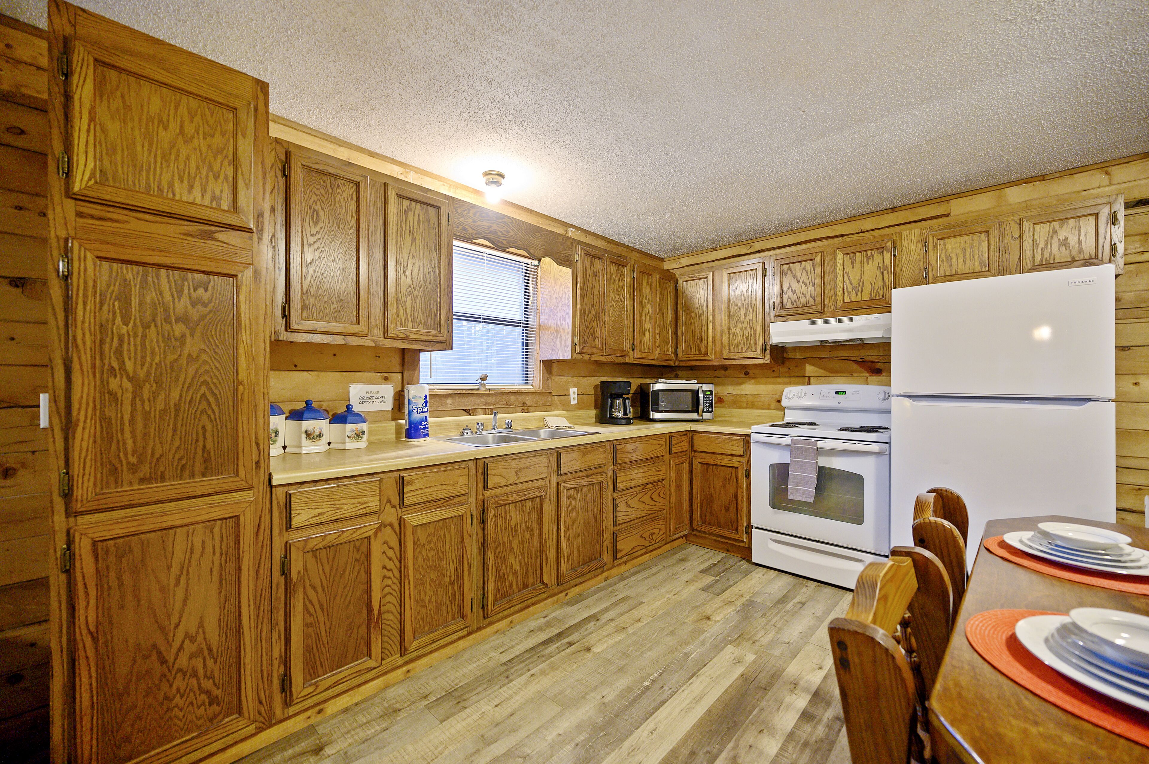 Una cocina con gabinetes de madera, un lavamanos, una estufa, un microondas y un refrigerador.