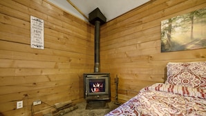 Una habitación acogedora con paredes de madera, suelo de piedra, cama con ropa de cama estampada, estufa de leña encendida y un cartel motivacional.