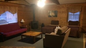 A cozy log cabin interior with a red sofa, a brown armchair, a wooden coffee table, and a fireplace.