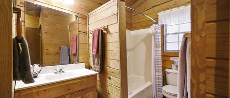 A wooden cabin bathroom with a sink, mirror, and a shower area.