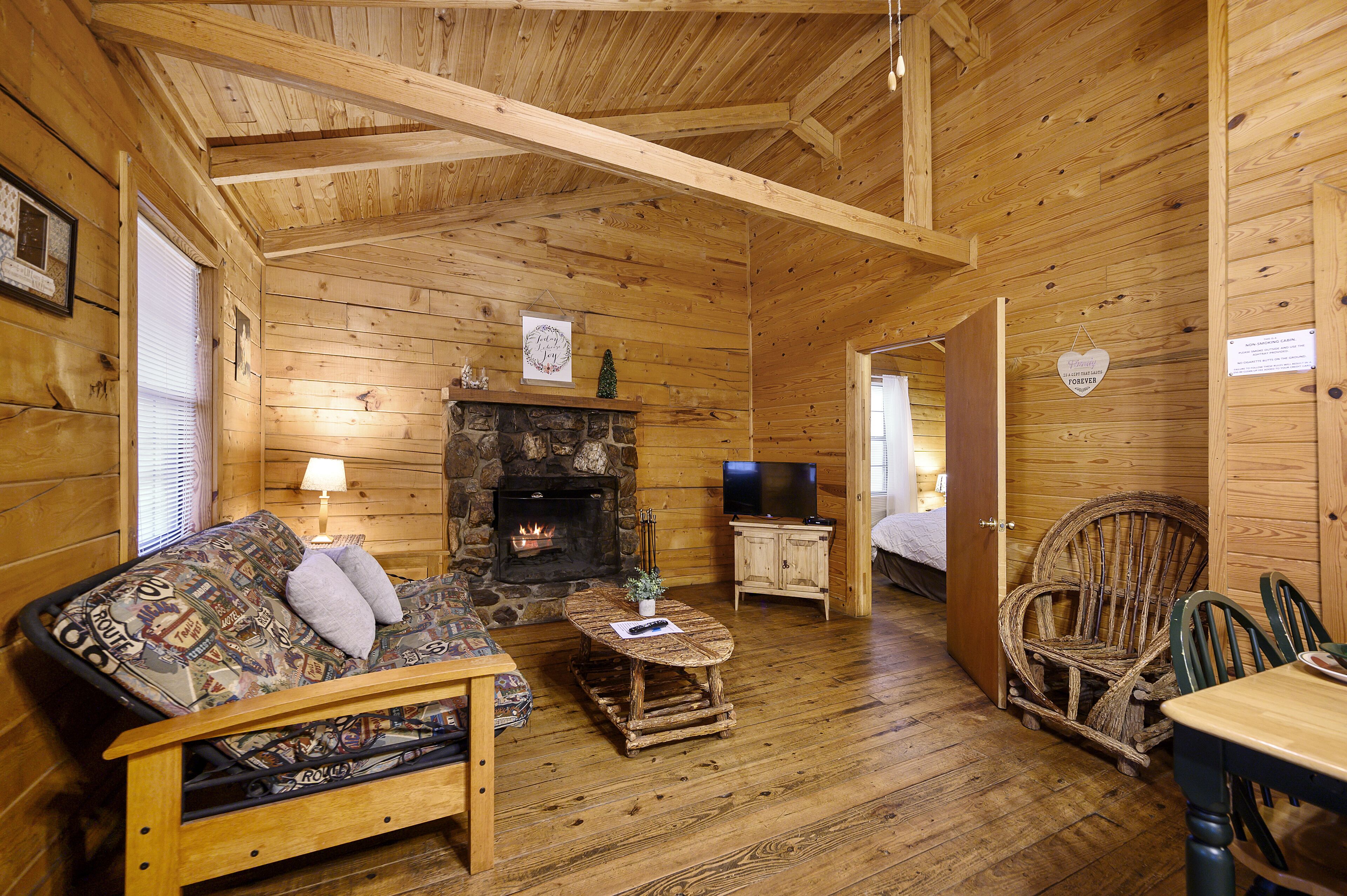 L’intérieur d’un chalet chaleureux, avec une cheminée en pierre, des meubles en bois et un téléviseur.