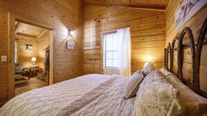 Een slaapkamer in een houten chalet met een bed, een raam met gordijnen en een spiegel aan de muur.