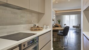 A modern kitchen with a built-in stove, oven, and a dining area with a table and chairs. - Chic n Bright 3 Bd Apt with Hilton View (Athens)