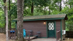 Eine rustikale Holzhütte mit grüner Tür, einer kleinen Veranda und zwei Stühlen, sowie ein blaues Kajak in der Nähe.