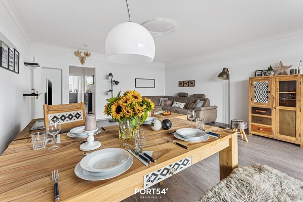 Een moderne eethoek met een houten tafel gedekt voor vier personen, een witte hanglamp en een rustieke kast met deurpanelen met patroon.