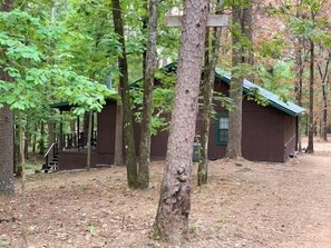 A rustic cabin with a wooden exterior, surrounded by dense trees and a covered deck area.