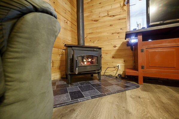 Ein gemütliches Zimmer mit Kaminofen, Holzwand und Fliesenboden.