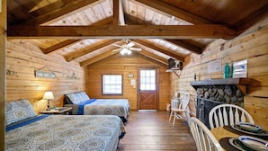 A cabin with two beds, a dining table, and a fireplace. - Sweet Pea Place | Sleeps 4 | Fireplace, Fire Pit & Near Beavers Bend (Broken Bow)