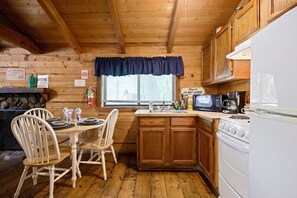 A wooden cabin kitchen with a dining table, chairs, a sink, a microwave, a stove, and a refrigerator.