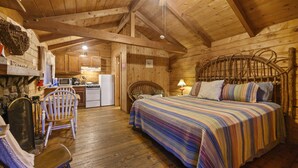 Una habitación acogedora de estilo cabaña con techo de madera, cama con manta a rayas, una silla y una pequeña kitchenette.