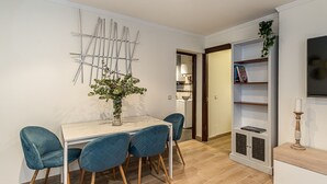 Un coin repas avec une table blanche, trois chaises bleues, une sculpture métallique décorative et une bibliothèque agrémentée d’une plante.