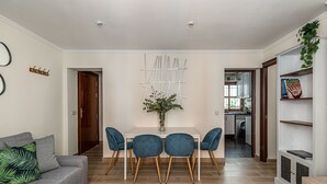 Un salon moderne avec un canapé gris, une table à manger entourée de quatre chaises bleues, un élément décoratif mural et une bibliothèque.