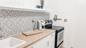 A kitchen with a white countertop, a sink, a stove, and a patterned backsplash. - Lovely Bohemian Apartment (Fort Lauderdale)
