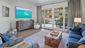 Amplia sala de estar con un televisor de pantalla plana grande, ventilador de techo y vista a una piscina y zona de estar exterior.