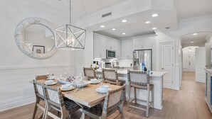 Una cocina moderna con armarios blancos, una mesa de comedor de madera y una lámpara colgante.