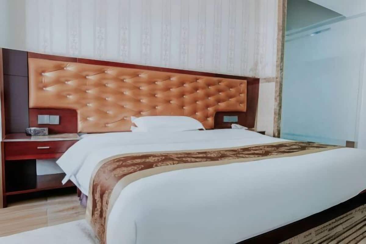 Habitació d'hotel amb un llit gran, un capçal de fusta, una taula de nit i una tauleta auxiliar.