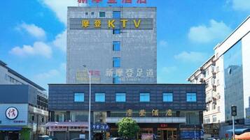 Un hôtel avec une enseigne indiquant la présence d’un karaoké, une devanture de magasin avec une enseigne pour un restaurant, et un ciel bleu azur.
