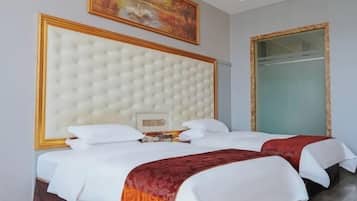 A hotel room with a large tufted headboard, two beds with white bedding, a red accent throw, a painting on the wall, and a large mirror.