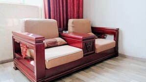 A wooden sofa with cushions in a room with a tiled floor and a red curtain. - Guangzhou New Modern Hotel (Shiling lisha squar) (Guangzhou)
