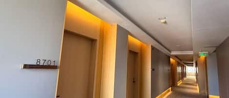 Corredor de hotel com portas numeradas 8701, piso com carpete e teto com iluminação embutida.