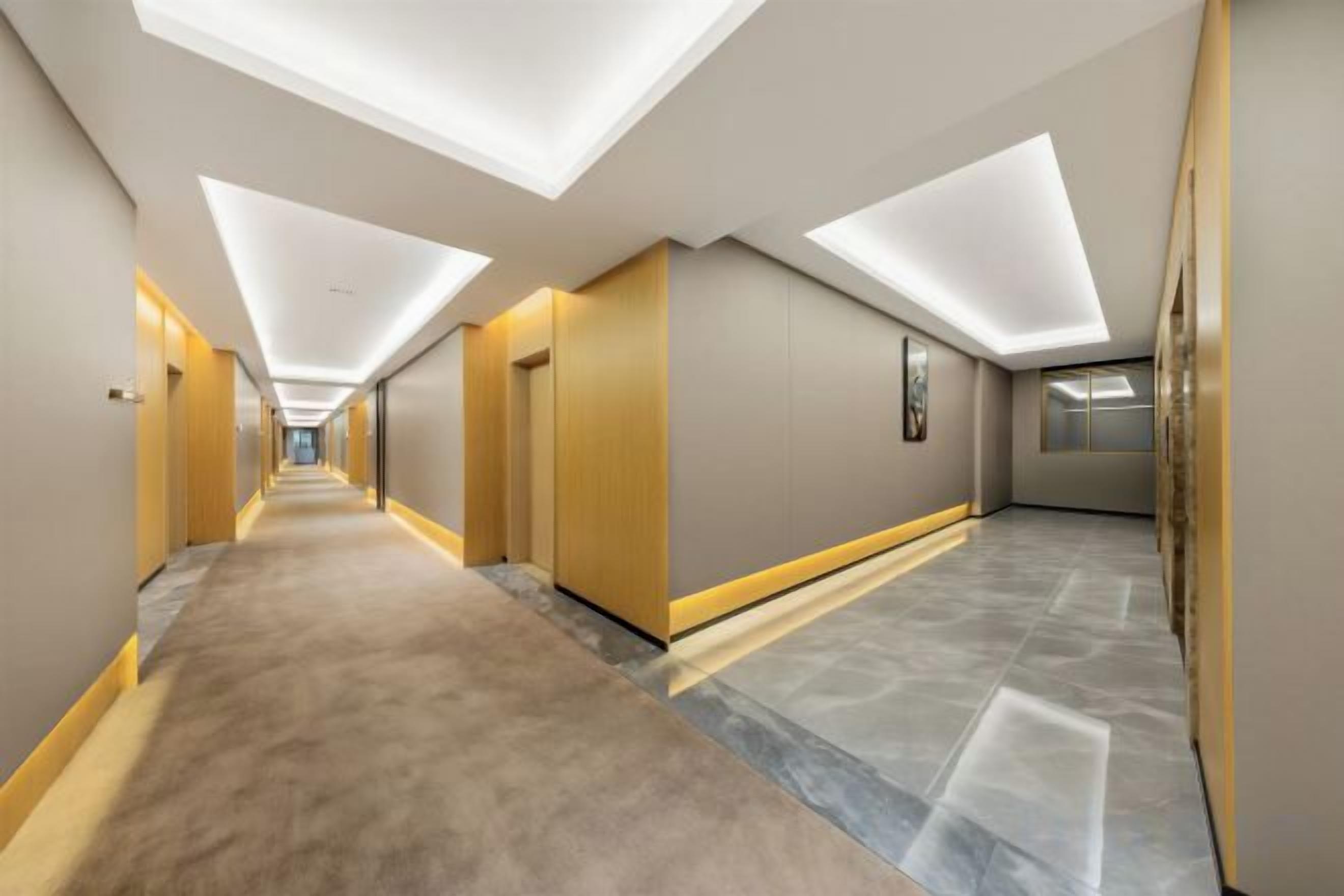Ein langer, schmaler Hotelkorridor mit Teppichboden, eingelassener Beleuchtung und modernem Design.
