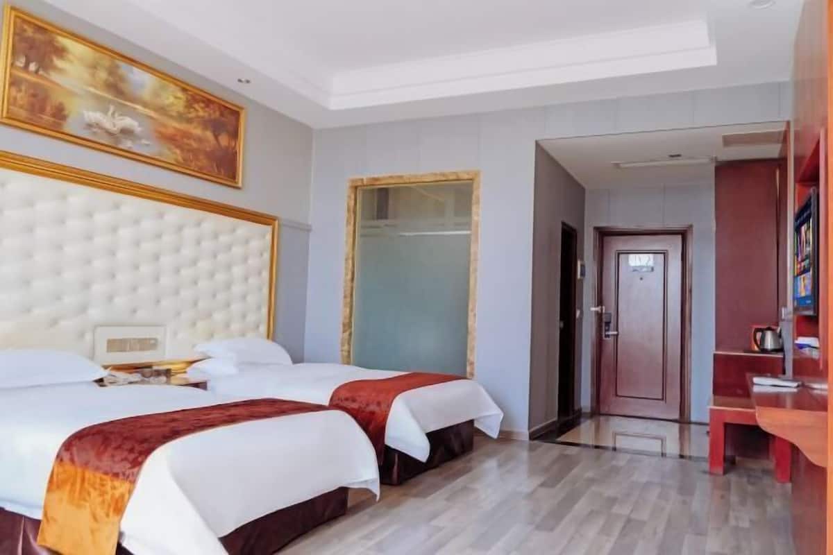 Una habitació d'hotel amb dos llits, una finestra gran, un quadre i una porta que dóna a una altra habitació.
