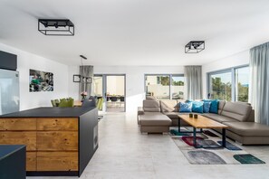 A modern apartment with a kitchen, dining area, and living room. There are large windows, a sofa, and a coffee table.