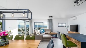 A modern living room with a wooden dining table, green chairs, a beige sofa, and a TV on a wooden stand. - Seaview Villa Big Blue with 32sqm heated pool, 4 bedrooms (Podstrana)