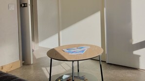 A small round wooden table with a glass top, positioned in a corner of a room with a white door and a light-colored floor.