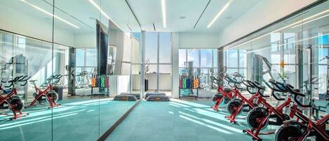 A modern gym with mirrored walls, rows of stationary bikes, and a central open space.