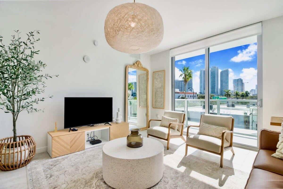 A modern living room with a large TV, comfortable seating, a round coffee table, and a city view through large windows.