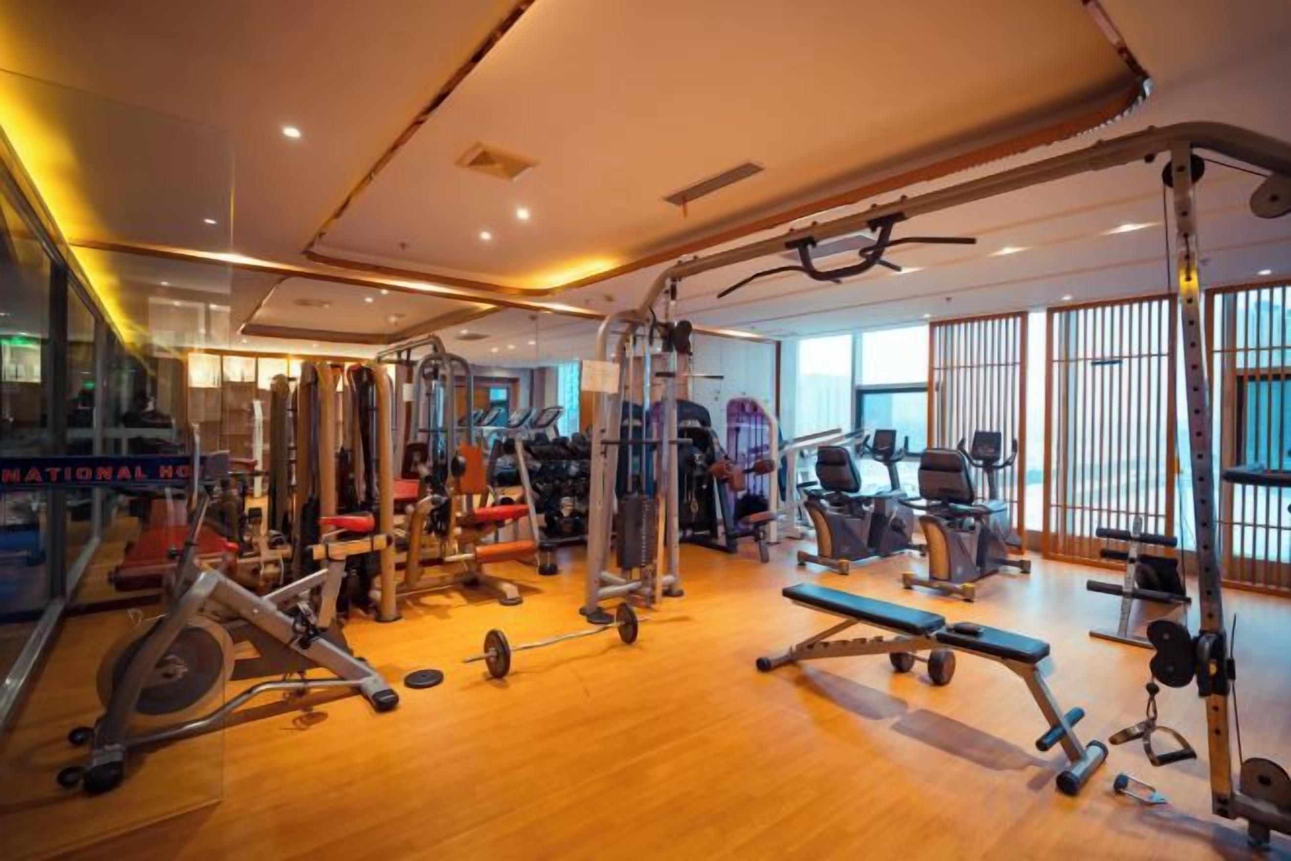 Un gimnasio con equipo de ejercicio variado, ventanas amplias y piso de madera.