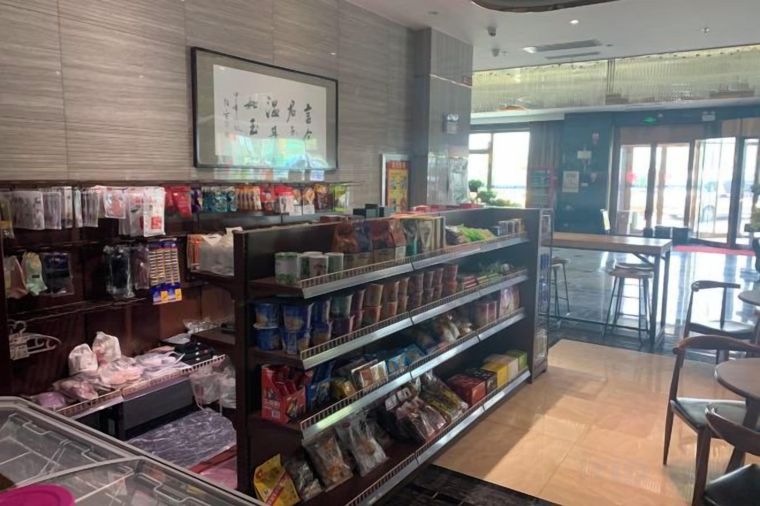 A retail store with shelves stocked with various products, a checkout counter, and a seating area with tables and chairs.
