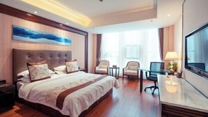A hotel room with a large bed, a desk, two chairs, a TV, and a painting on the wall. - Henglong International Hotel (Karamay)