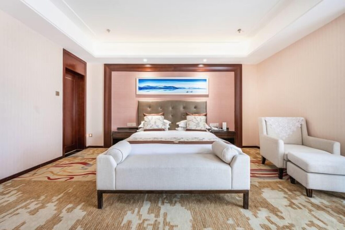 Habitación de hotel con una cama grande, zona de estar, un cuadro en la pared y suelo alfombrado.